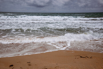 Sea waves beating against the sandy shore. Stormy ocean landscape. Vacation and travel.