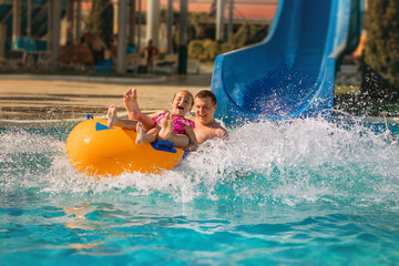 Summer holidays on a sunny day in an outdoor water park. A father and a child ride on a rubber...