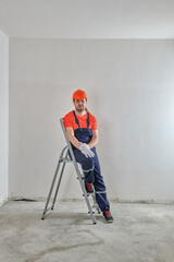 in a blue overalls, a foreman stands at a stepladder in a helmet