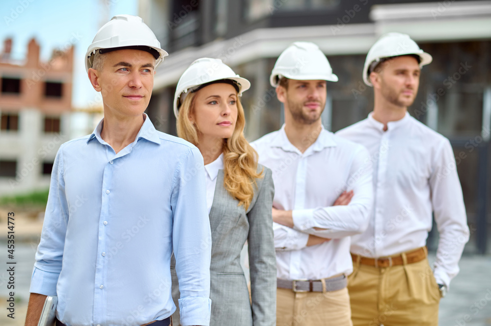 Wall mural Four adult people in hardhats standing on the building site