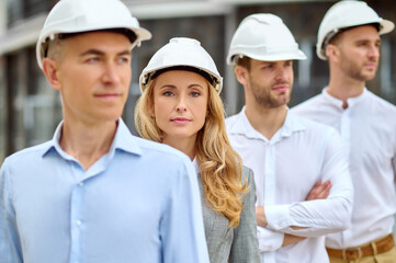 Woman supervisor and builders in hardhats standing outdoors