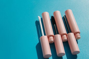 pink tubes of cosmetics and brushes lie on a blue background. Copy space. Closed tubes of lipstick, liquid lip gloss, mascara, eyeliner
