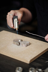 Hands of jeweler soldering silver ring with torch on board in workshop