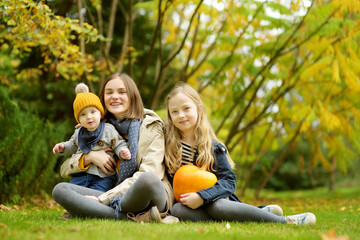 Fototapeta premium Two cute young girls and their baby brother holding a small pumpkin on sunny autumn day. Kids trick or treating on Halloween.