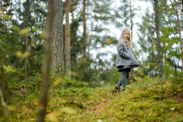 Naklejka na ściany i meble Cute young girl having fun on beautiful autumn day in a forest. Active family leisure with kids.