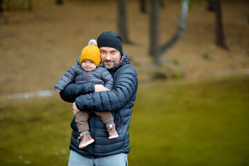 Cute little baby boy in his fathers arms. Dad and son having fun on cold autumn day in city park. Son being held by his daddy.