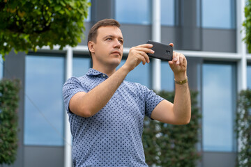 Caucasian tourist man takes photo on mobile phone. Men on street photographing with smartphone. Handsome man takes photo using smart phone while walking outdoors