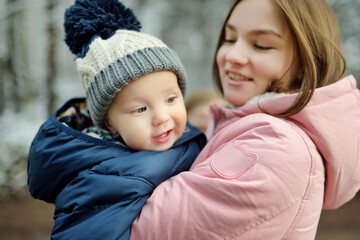 Obraz premium Big sister and her baby brother having fun outdoors. Young girl holding her baby boy sibling on winter day. Kids with large age gap