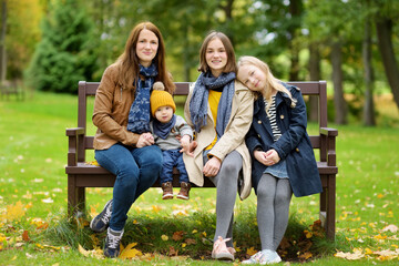 Family of four having fun during forest hike on autumn day. Young mother and her three children exploring nature.