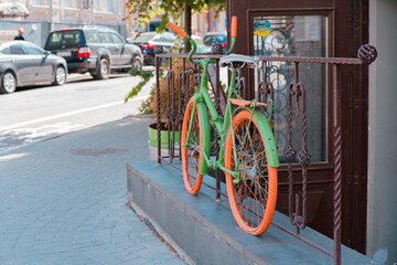 Fototapeta na wymiar Colourful green and orange bicycle stands on the fence near entrance as a decoration. Decor. City. Style. Building. Outdoor. Urban. Shop. Cafe. Restaurant