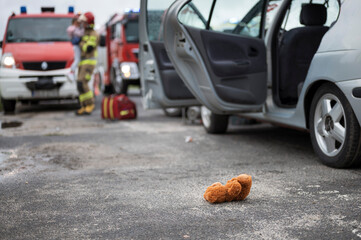 Car accident - teddy bear lying on the road and baby in lifeguard hands in the background.
