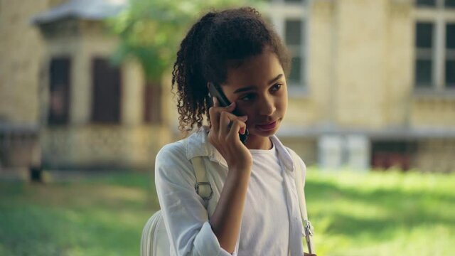 Scared biracial teen girl talking phone, standing alone in street, calling help