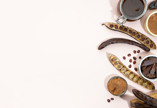 Organic carob pods, powder and carob molasses on a beige background, locust bean healthy food, Ceratonia siliqua harnup. Natural vegan eating. creative food background. Copy space.Flat lay.Top view