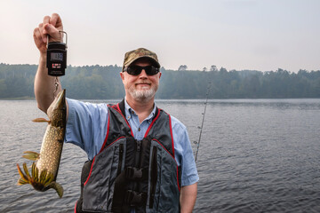 A beard man with smile is holding a northern pike