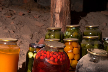 Glass jars with canned vegetables, fruits and berries are in the village cellar. Close-up. Old banks.. The foreground is yellow, red and a jar covered with dust.