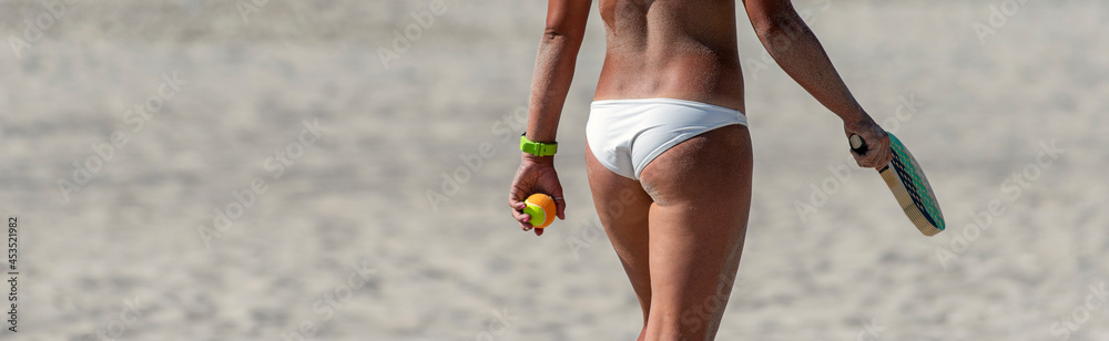 Wall mural Young girl playing beach tennis on sand. Professional sport concept. Horizontal sport poster, greeting cards, headers, website.