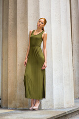 Dressing in a green Maxi Tank Dress, creamy high heels,  a young fashion black girl is standing  by a huge column, relaxing and thinking.