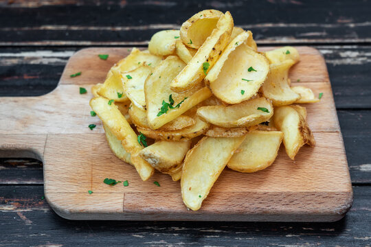 Fried potatoes cut with herbs on a wooden kitchen board. Close-up.