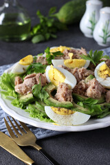 Healthy salad with avocado, tuna, eggs and cucumbers on a white plate on a dark gray background. Vertical format