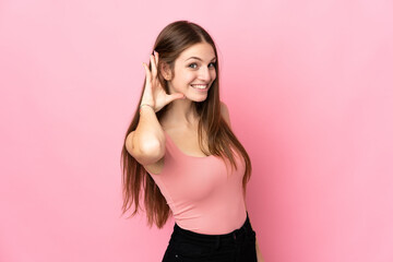 Young caucasian woman isolated on pink background listening to something by putting hand on the ear