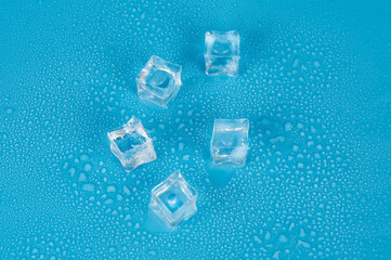 Five cubes of melting ice on a blue background in water drops.