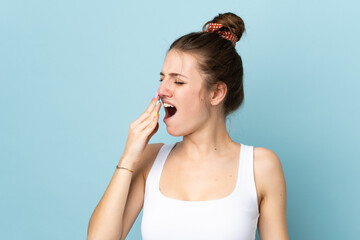 Young caucasian woman isolated on blue background yawning and covering wide open mouth with hand