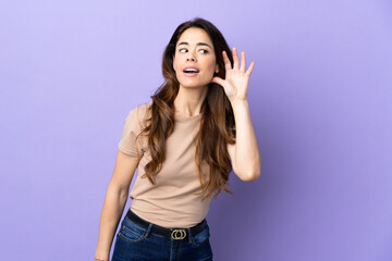 Woman over isolated purple background listening to something by putting hand on the ear