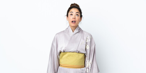 Woman wearing kimono over isolated background looking up and with surprised expression