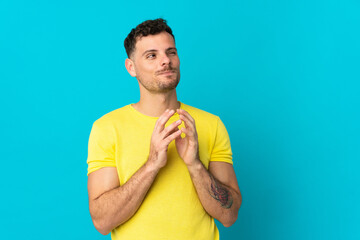 Young caucasian handsome man isolated on blue background scheming something