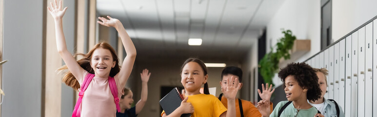 cheerful multicultural children waving hands in school corridor, banner