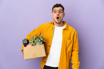 Young caucasian man making a move while picking up a box full of things isolated on purple...