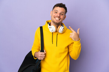 Young sport caucasian man with bag isolated purple background giving a thumbs up gesture