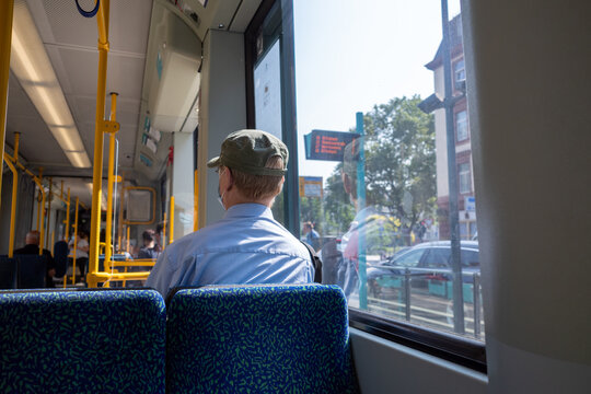 Interior and selected focus view at the back of male passenger with face protection mask who sit in light rail tram or train in Germany during epidemic of COVID-19 virus with new normal concept.