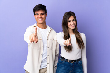 Young couple over isolated purple background showing and lifting a finger