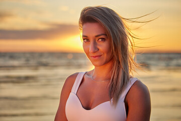 Naklejka premium Young woman stands on coast during sunset in summer.