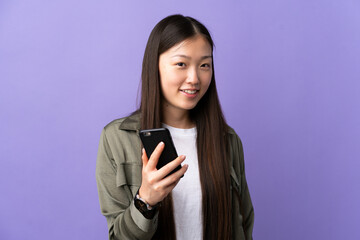 Young Chinese girl using mobile phone over isolated purple background with happy expression