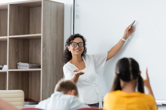 Smiling African American Teacher Pointing At Erase Board And Pupils During Lesson