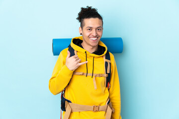 Young mountaineer man with a big backpack over isolated blue background making phone gesture