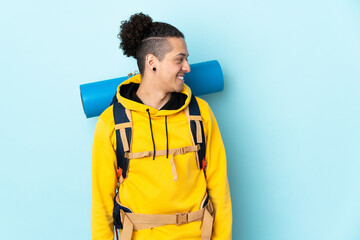 Young mountaineer man with a big backpack over isolated blue background looking to the side