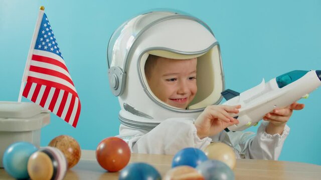 Child playing at home in an astronaut, portrait of a little boy 5 years old in an astronaut costume, smiling happy child looking at the camera,close-up, pilot holding an American flag,travel to space
