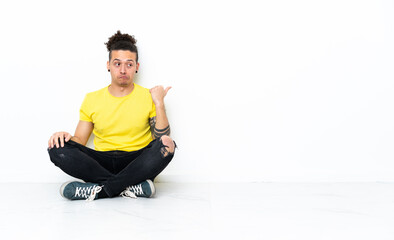 Caucasian man sitting on the floor unhappy and pointing to the side