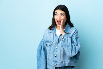 Young brunette girl over isolated blue background whispering something with surprise gesture while looking to the side - obrazy, fototapety, plakaty