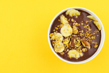 Brazilian açai in a white bowl with banana, granola and chestnuts.
