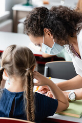 african american teacher helping schoolgirl during lesson