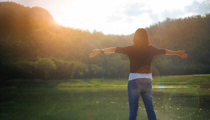 Young woman is standing turned back and raised arms to relax with the beauty of nature and morning sunlight.