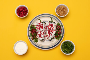 Chiles en Nogada, a traditional dish from Puebla with the addition of walnut cream, pomegranate seeds and parsley and some ingredients on yellow background