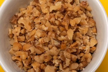 Close up of peeled chopped walnuts in a white bowl on yellow background