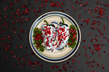 Chile en Nogada, a traditional dish from Puebla with the addition of walnut cream, pomegranate seeds and parsley on black background with pomegranate grains