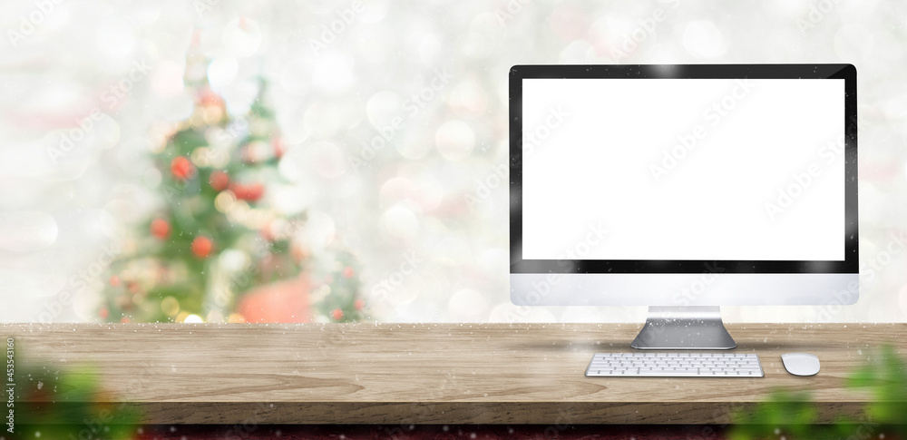 Aufkleber Merry Christmas with blank desktop computer on wood table at blur bokeh xmas tree decor with string light background,Winter banner backdrop for holiday greeting card advertise promotion on online