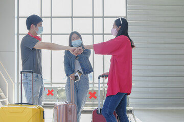 Asian young traveler group wearing protective face mask and fist bump greeting together at public terminal area. COVID-19 awareness and new normal travel lifestyle concept. Selective focus.